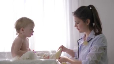 Sağlıklı çocukluk, profesyonel aile doktoru kadın çocuk kliniğe yakın parlak ışıkta muayene ediyor.