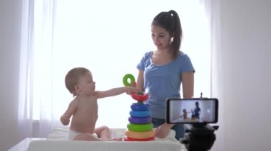 Modern pazarlama, anne vlogger ile neşeli çocuk eğitim oyuncakları tarafından oynanırken cep telefonuyla sosyal ağlardaki takipçiler için çevrimiçi video blogu kaydediyor.