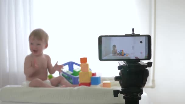 Blog about child development, cute kid boy in unfocused play with educational toys while video recording on mobile phone for subscribers in social networks — Stock Video