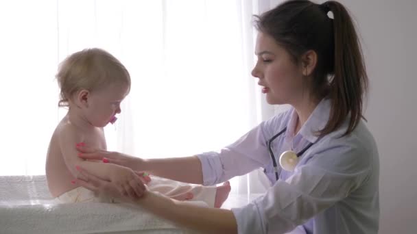 Klein kind bij dokter op medische controle, professionele kinderarts vrouw onderzoekt zoete baby jongen in helder natuurlijk licht in het ziekenhuis — Stockvideo