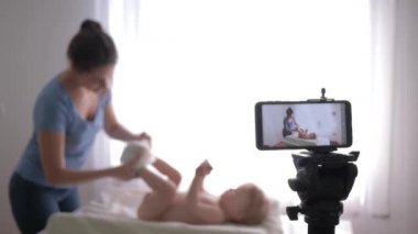 Genç anneler için eğitici video blogu, genç anne vlogger bebek bezini küçük çocuk olarak değiştirirken takipçiler için kapalı telefon ile eğitim videosu kaydediliyor.