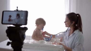 E-öğrenme, steteskoplu doktor kız öğrencilere cep telefonuyla sosyal medyada canlı yayın yapan çocuğun kalp atışlarını ve nefesini kontrol ediyor.