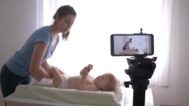 Modern blog yazarlığı, genç anne blogcu, abonelerin eğitim videolarını canlı yayında kaydederken bebek bezi değiştiriyor.