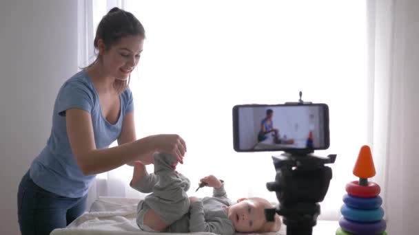 Blog yazarlığı, modern anne vlogger çocuk kıyafetlerini değiştirirken sosyal ağlardaki takipçiler için cep telefonundan eğitim videosu kaydediliyor. — Stok video