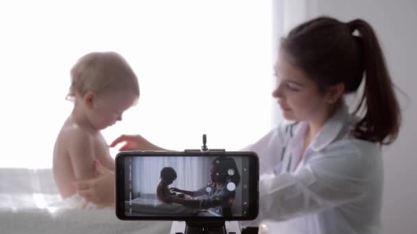 Blogging, popular vlogger médico femenino filmando nuevo episodio para vlog en el teléfono inteligente durante el examen médico del bebé para los seguidores — Vídeo de stock