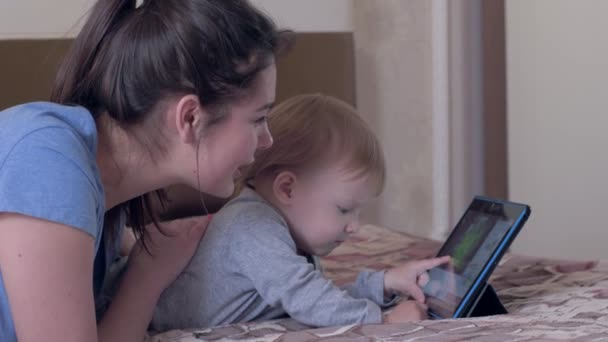 Onderwijs technologieën, nieuwsgierig baby jongen met gelukkig mama veel plezier met digitale tablet liggend op bed op kamer — Stockvideo