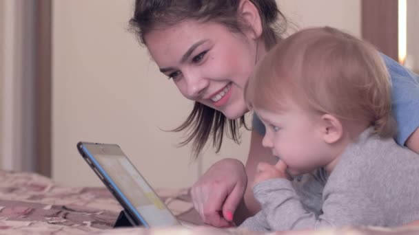 Moderne ontwikkeling van het kind, mooie peuter jongen met gelukkig moeder rusten met digitale tablet liggend op bed binnen — Stockvideo