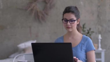 Gözlüklü işkolik bir kadın dizüstü bilgisayarda yazı yazıyor ve evde yakın plan iş sırasında ekrana bakıyor.