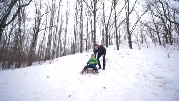 Fim de semana de inverno da família, menino desliza rapidamente para baixo no trenó de uma neve coberto de montanhas — Vídeo de Stock