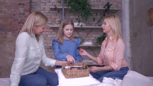 Barn makeup, lycklig mor med vuxen dotter tillämpa kosmetika på vacker liten flicka med hjälp av speciella borstar under fritid på sängen hemma — Stockvideo