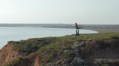 Dağın tepesindeki akro yogada, sportif kız deniz ve gökyüzünün arka planındaki çayırda erkek arkadaşının bacaklarının üzerinde dengede duruyor.