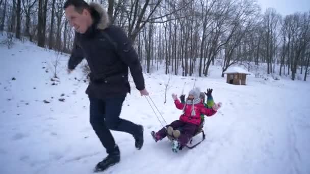 Зимний сезон в лесу, отец тянет своих детей на санях по снежной дороге — стоковое видео