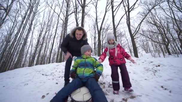 Дети веселятся с отцом, бегают и катаются на санках в снежном лесу в зимние выходные — стоковое видео