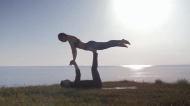 Akroyoga, yoga yapan iki sporcu, gün batımı arka planında çiftler halinde, genç çift dağ üzerinde esneme egzersizi yapıyor.