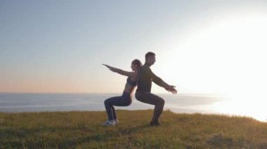 Atletik çift gün batımında güzel bir manzaraya karşı aynı anda dağda çömeliyor.