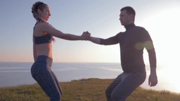 Mode de vie actif, couple athlétique tenant la main et simultanément accroupi à la nature — Video