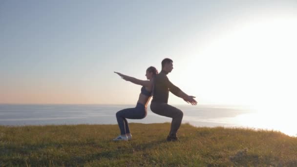 Atletiska par tillbaka till ryggen samtidigt huka på berget mot ett vackert landskap under solnedgången — Stockvideo