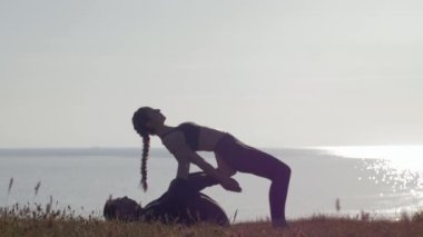 Açık havada meditasyon, kadın ve erkek deniz ve günbatımının arka planında dağda çift yoga yapıyor.