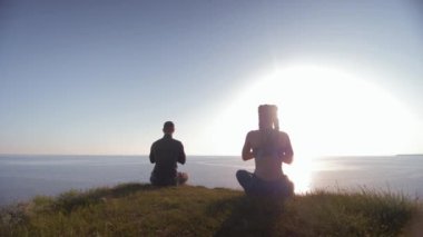 Manevi dünya, dağın tepesinde oturan kadın ve erkek, karadaki nilüfer pozisyonunda meditasyon yapan denize bakıyor.