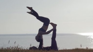 Doğa antremanı, sportif çift deniz ve gün batımının arka planında çayırda akro yoga yapıyor.