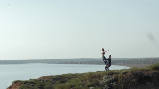 Meditation på naturen, par utövar acro yoga, flicka ett ben balanserar på fotspår av hennes manliga partner på bakgrunden av hav och himmel — Stockvideo