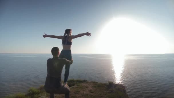 Meditation on background of sea, man and woman doing yoga exercises with beautiful pose on mountain during sunset — ストック動画