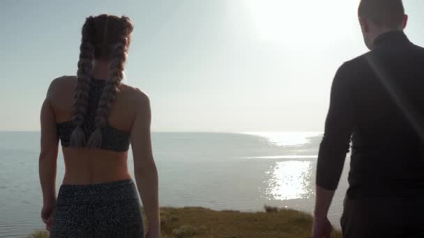 Okamžik harmonie, sportovní milující pár držící se za ruce sledující západ slunce u vody stojící na hoře společně na pozadí oblohy — Stock video