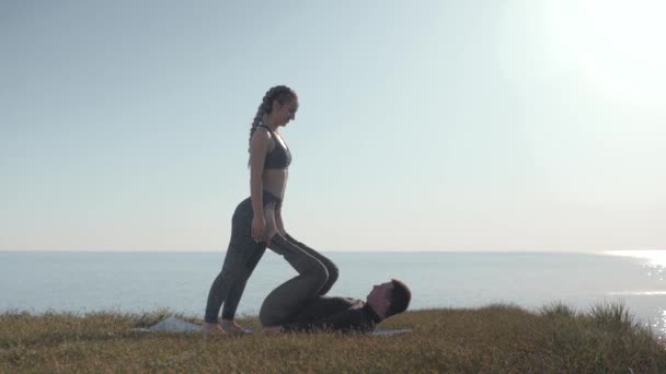 Pareja deportiva practicando acro yoga en la montaña, acrobat femenino es el equilibrio en las piernas de su pareja masculina en el fondo del cielo — Vídeos de Stock