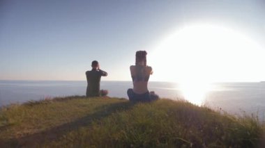 Yoga yaşam tarzı, gün ışığında genç bir adam ve kadın dağın tepesinde oturmuş karadaki nilüfer pozisyonunda meditasyon yapan denizlere bakıyor.