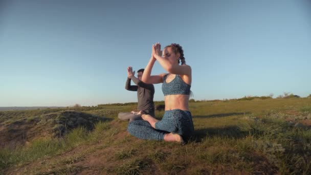 Ioga estilo de vida, mulher esportiva e homem no prado juntos meditando na posição de lótus no fundo do céu — Vídeo de Stock