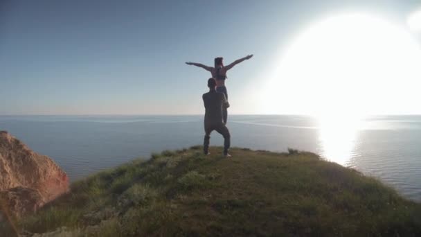 Yoga çalışmaları, kollarını kaldırmış spor kızı deniz ve gökyüzünün arka planında erkek arkadaşının bacaklarında dengede duruyor. — Stok video