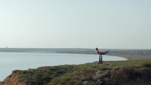 Yogautövande, sportig flicka balanserar på benen på hennes manliga partner på berget på bakgrund av flygande fågel och himmel — Stockvideo