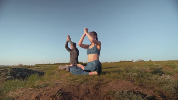 Jóga náboženství, sportovní pár spolu medituje v lotosové poloze na louce na pozadí oblohy — Stock video