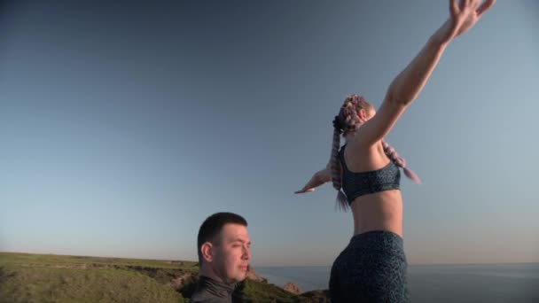 Yoga sport, athletic woman with arms raised is balancing on legs of male partner on background of beautiful nature — Stock Video