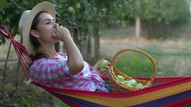 Garden, young rustic woman with basket of apples resting in hammock — Stock Video