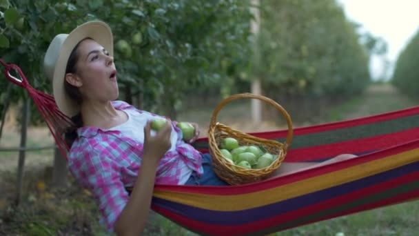 Pihenés a kertben, boldog lány fekszik függőágyban, és eszik almát a természetben betakarítás közben — Stock videók