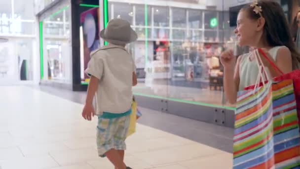 Viernes negro, niños alegres con bolsas de compras en la mano están contentos con las nuevas compras en el centro comercial — Vídeos de Stock