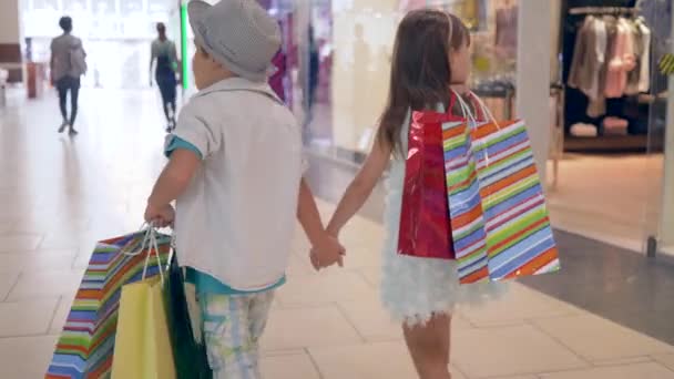 Enfants en shopping, amis enfants élégants avec des achats entre les mains passant par les vitrines au centre commercial après l'achat dans les boutiques chères — Video