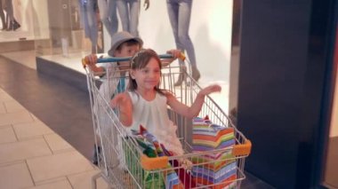Çocuklar alışveriş günü, olumlu duygusal çocuklar alışveriş merkezlerinde alışveriş arabalarında eğleniyor ve mağaza vitrinlerinin önünden geçiyorlar.