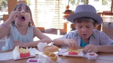 Yiyin, neşeli küçük oğlan ve kız abur cuburla oynayın ve fast food kafede öğle yemeği yerken komik suratlar yapın.