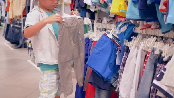 Мальчик покупатель выбирает новую одежду в магазине моды во время сезонных скидок — стоковое видео