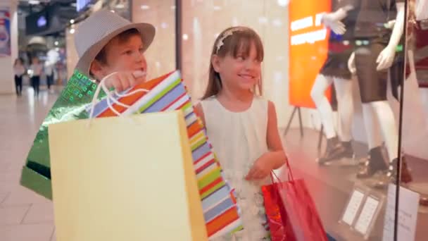 Venda sazonal, crianças amigas alegres com pacotes de compras passam por vitrines com manequins em boutique, texto aparece em uma frase clipe últimos dias de venda e descontos de palavra "vendas fora de temporada " — Vídeo de Stock