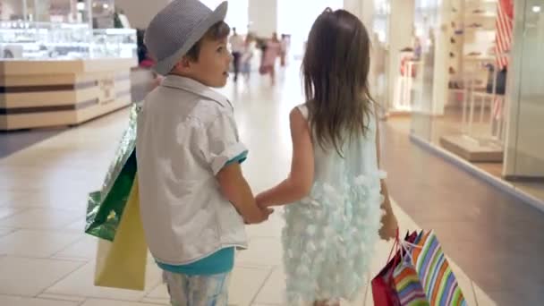 Vente de courses, petit frère avec soeur avec beaucoup de paquets marchant ensemble tenant la main au centre commercial après le shopping — Video