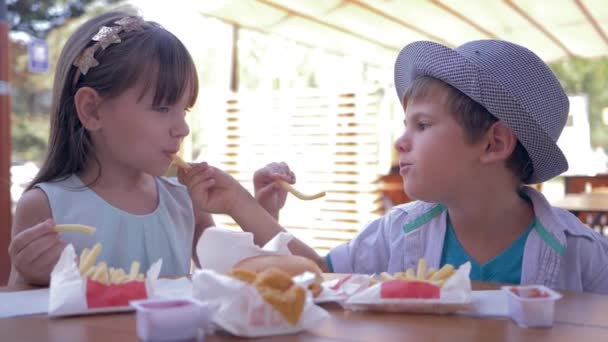 Cura dei bambini, bambini adorabili che si nutrono a vicenda fast food seduti a tavola nel caffè di strada — Video Stock