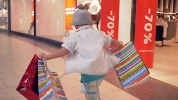 값비싼 옷을 사고 난 뒤, 손에 포장을 들고 있는 어린이가 패션 쇼핑 센터를 지나간다 — 비디오