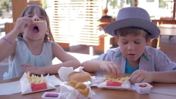 Игра с едой, веселый маленький мальчик и девочка играть с нездоровой едой и делать смешные лица во время обеда в кафе быстрого питания — стоковое видео