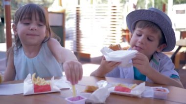 fast food in Street Cafe, hungry children eat french fries and hamburger sitting at table during lunch
