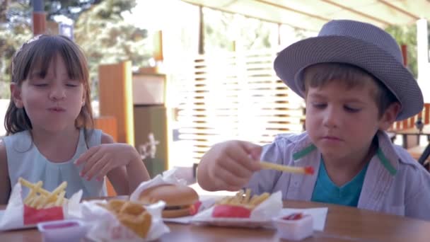 Comida para llevar, amigos felices niños comiendo papas fritas con salsa y hamburguesas en la cafetería de la calle durante el almuerzo — Vídeos de Stock