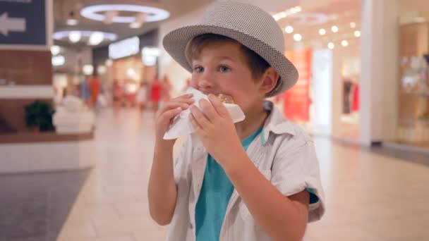 Children food, cute happy kid into Hat eating chocolate doughnut in shopping mall — Stock Video