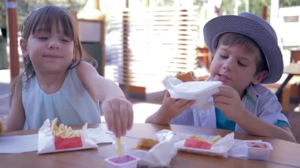 Фастфуд в уличном кафе, голодные дети едят французские фрикадельки и гамбургеры, сидя за столом во время обеда — стоковое видео